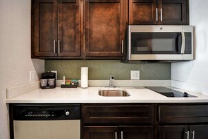 Una cocina con armarios de madera oscura, un microondas de acero inoxidable, un lavavajillas y un fregadero.