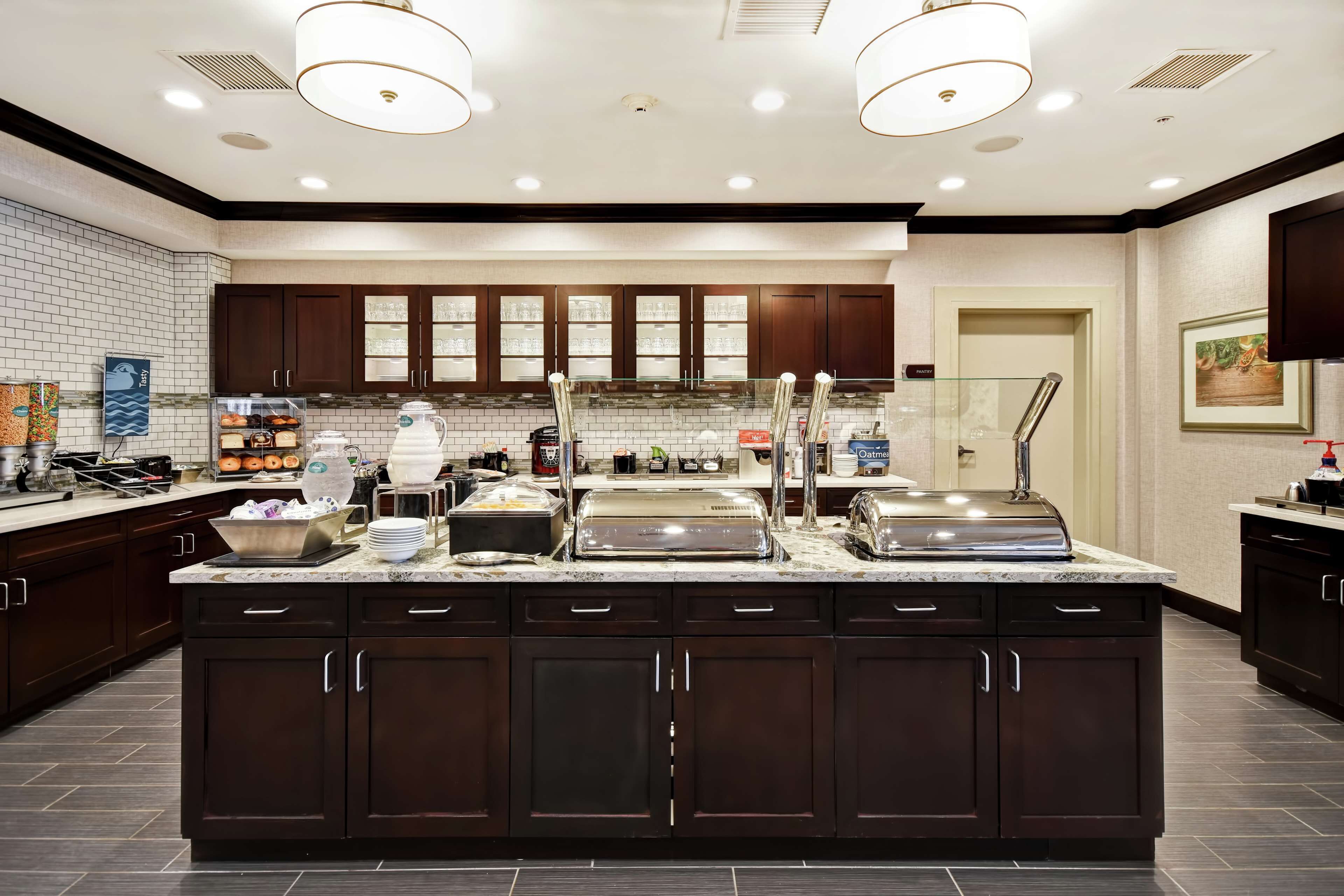 A modern kitchen with dark wooden cabinets, a marble countertop, and a central island with food dispensers.