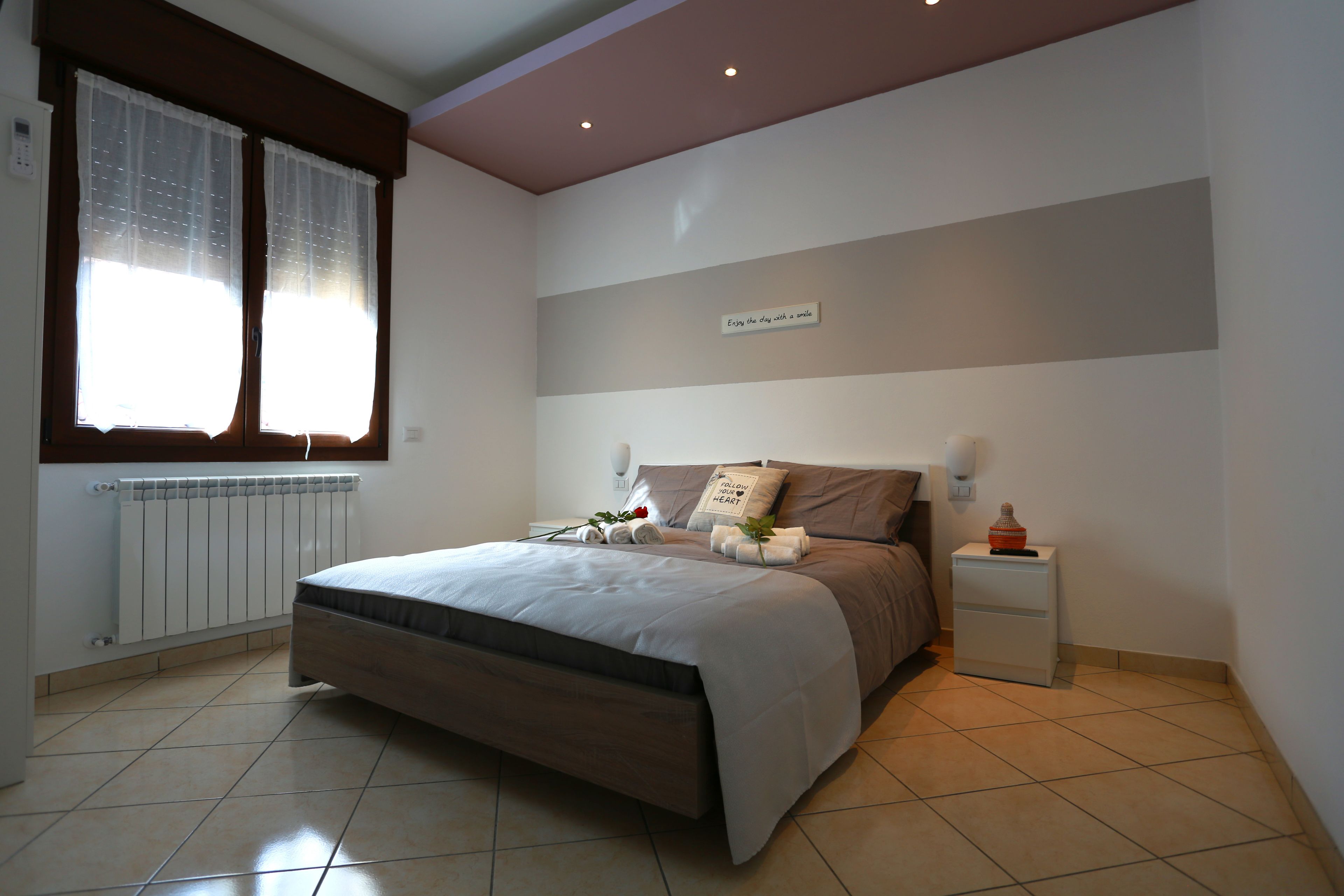 A bedroom with a bed, a nightstand, a wall-mounted lamp, and a window with curtains.
