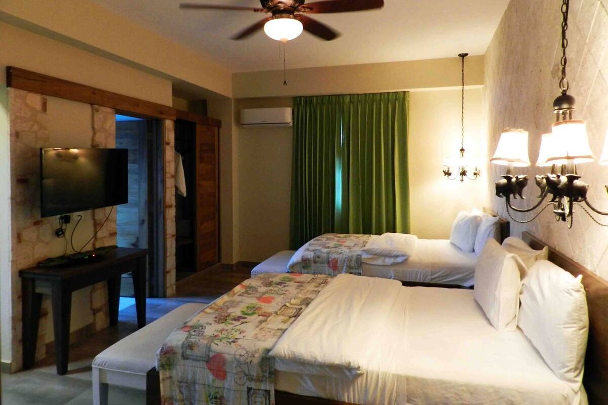 A hotel room with two beds, a ceiling fan, a TV, a desk, and a green curtain.