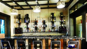A bar area with a long counter, multiple shelves of liquor bottles, and four metal bar stools. - MON Hotel Boutique (Constanza)