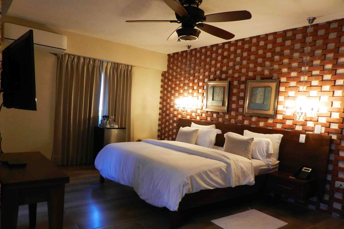A hotel room with a bed, a nightstand, a TV, a ceiling fan, and a brick-patterned wall.