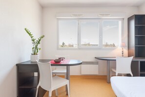 A small, modern room with a bed, a desk, and a chair. There is a window with a view of buildings outside. - City Résidence Marcy l'Etoile (Marcy-l'Etoile)