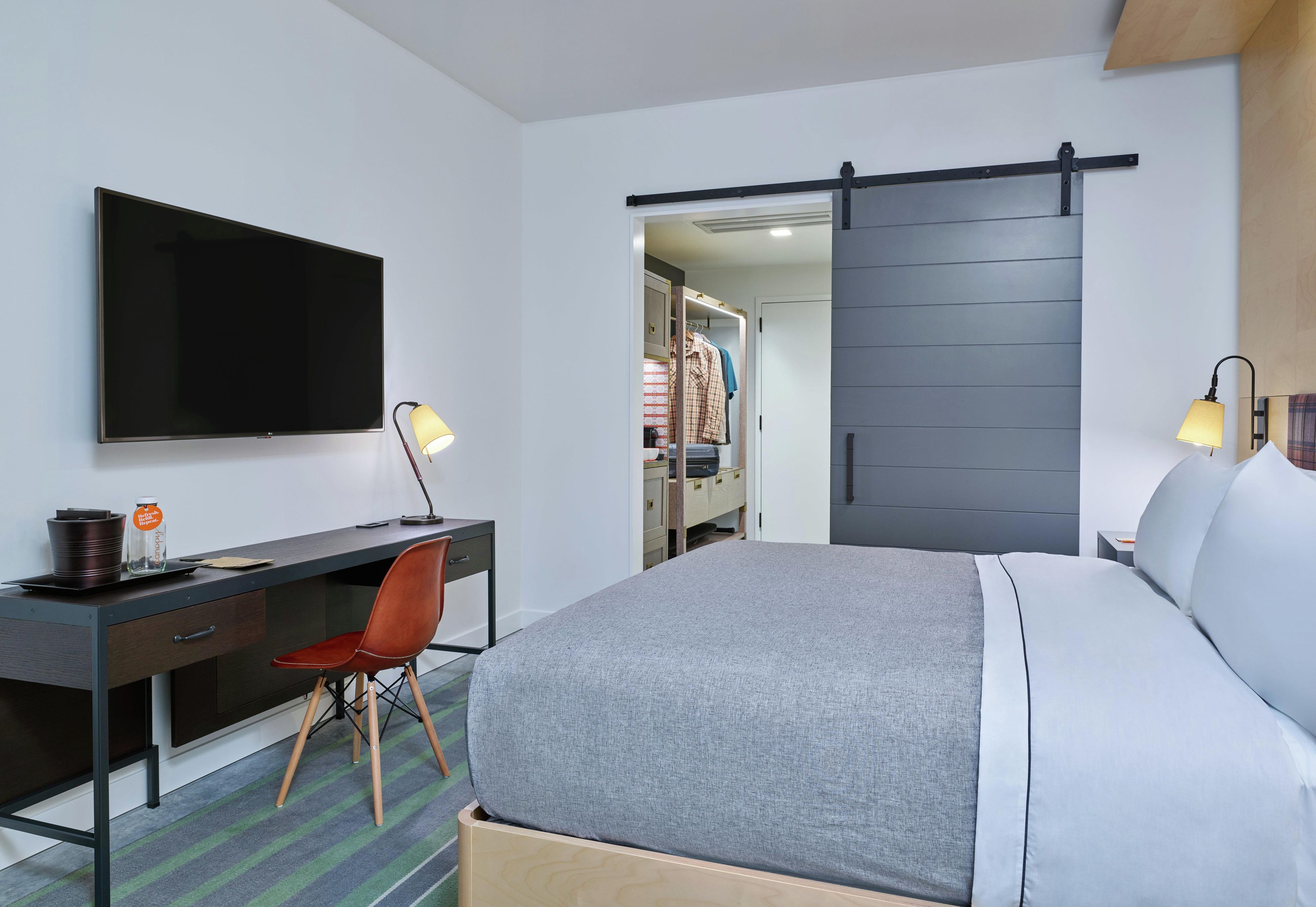 Una habitación de hotel con cama, escritorio y silla, televisión y armario con puerta corredera.