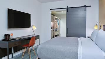 Una habitación de hotel con cama, escritorio y silla, televisión y armario con puerta corredera.