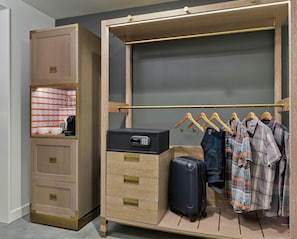 A walk-in closet with a built-in safe, a hanging rack with clothes, and a suitcase. - Canopy by Hilton Portland Pearl District (Portland)