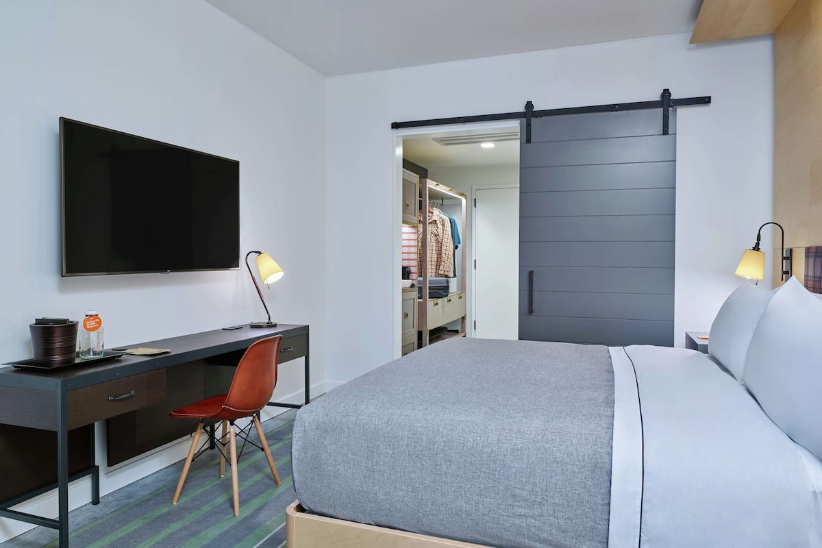 A hotel room with a bed, a desk with a chair, a TV, and a sliding closet door.