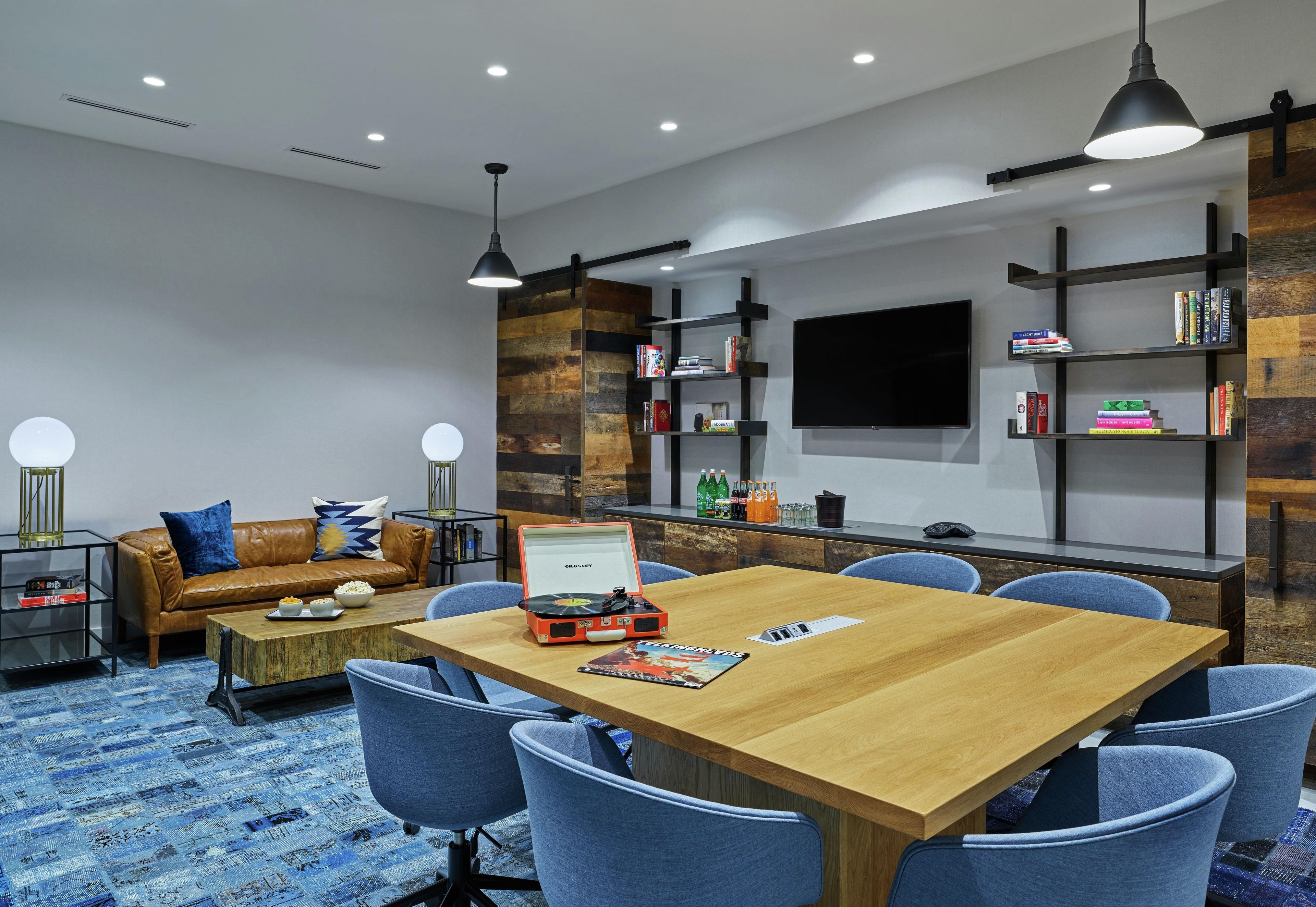 Uma sala de conferências moderna com uma mesa de madeira, cadeiras azuis, um sofá e estantes.