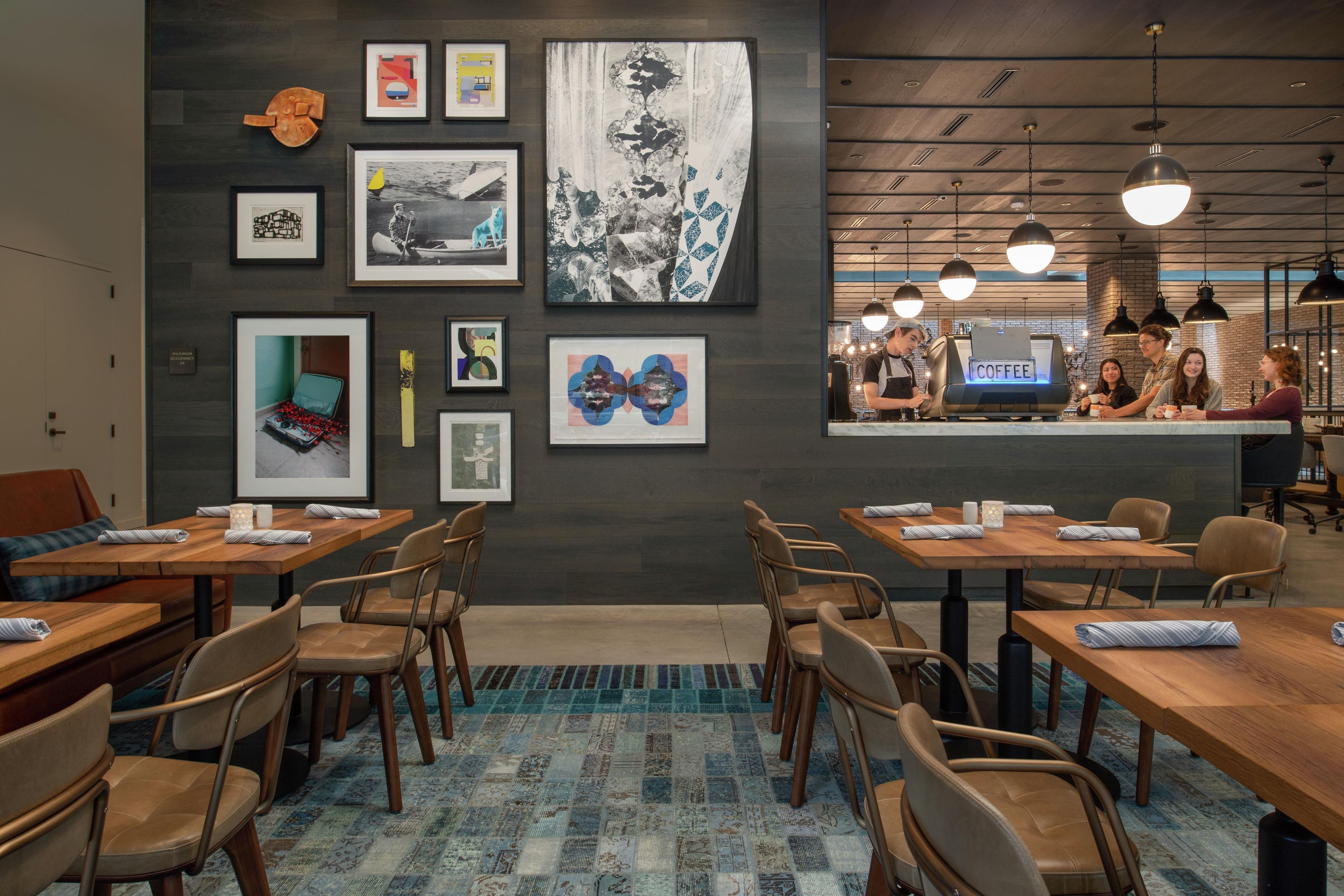 Una cafeteria moderna amb taules i caires de fusta, una barra de cafè i obra d'art a les parets.