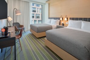 Habitación de hotel con dos camas, un escritorio, una silla y un ventanal con cortinas.