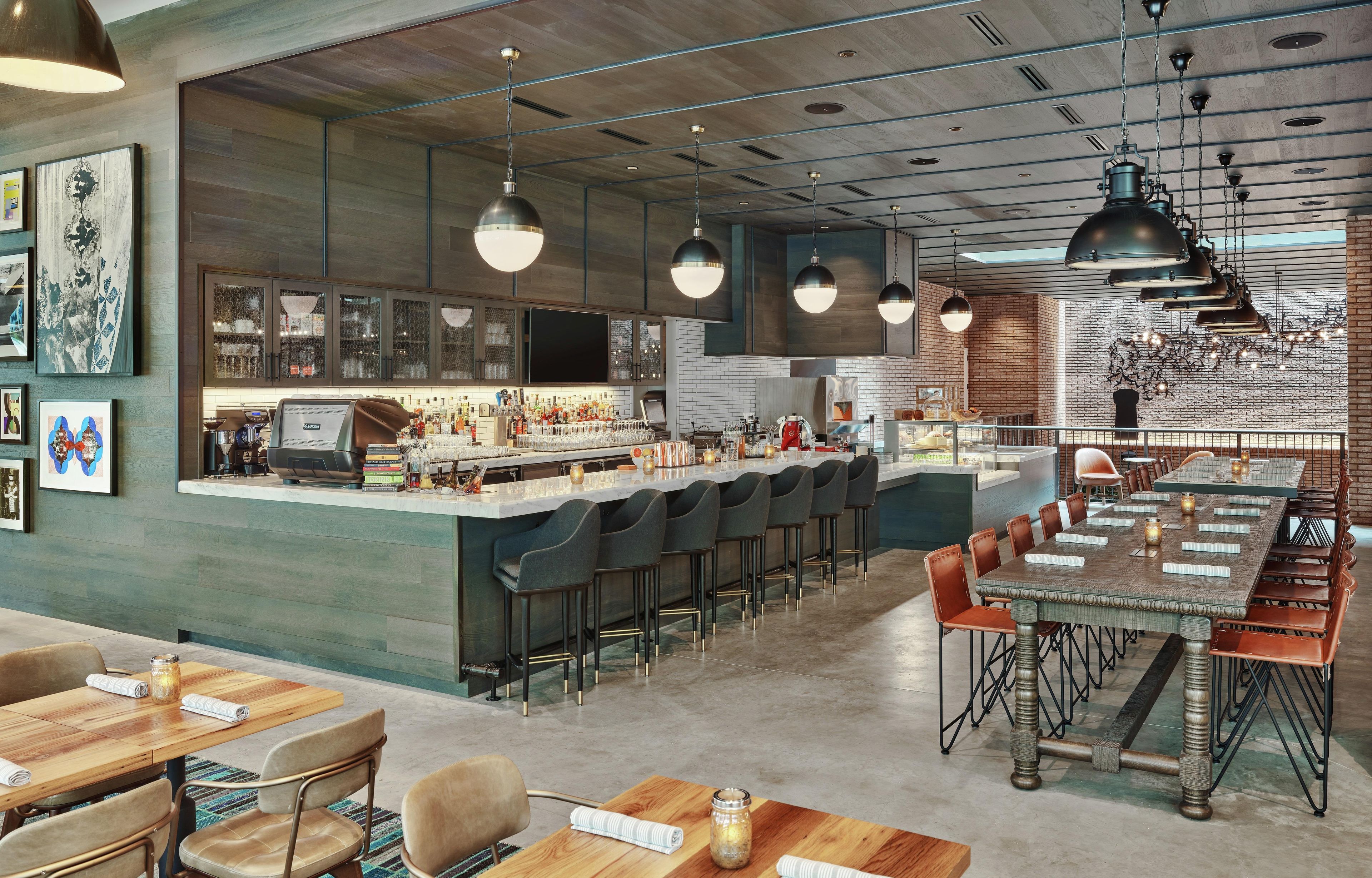 Un área de bar moderna con una barra larga, taburetes y un espacio de estar con mesas y sillas.