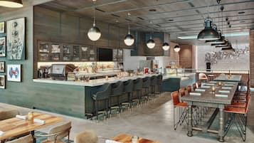 Un área de bar moderna con una barra larga, taburetes y un espacio de estar con mesas y sillas.