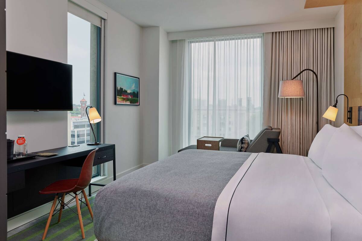A hotel room with a large bed, a desk with a chair, a TV, and a window with curtains.