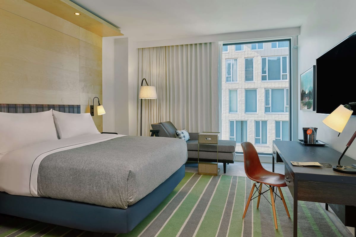A hotel room with a large bed, a desk, a chair, a laptop, and a window with curtains.