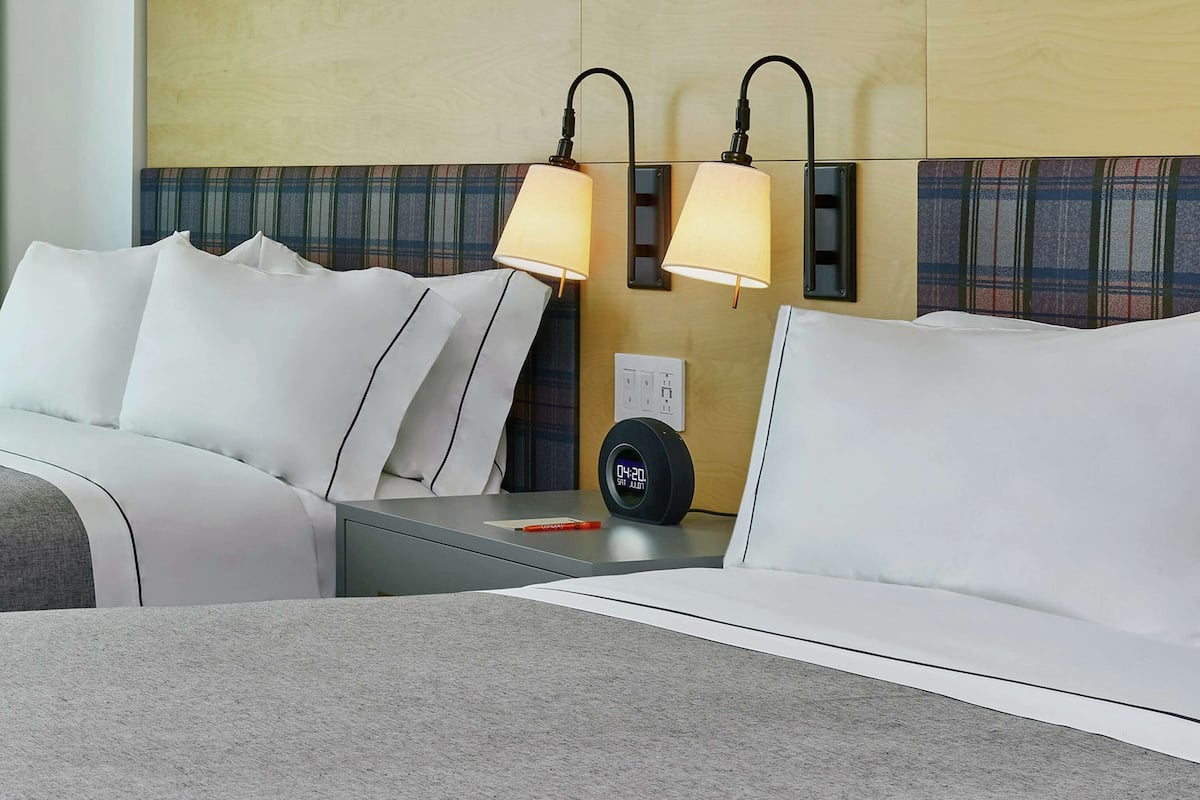A hotel room with a bed, two bedside lamps, a clock, and a nightstand.