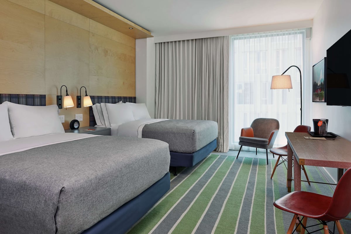 A hotel room with two beds, a desk, a chair, a lamp, and a TV.
