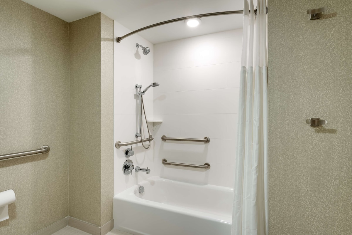 A modern bathroom with a walk-in shower, grab bars, and a white bathtub.