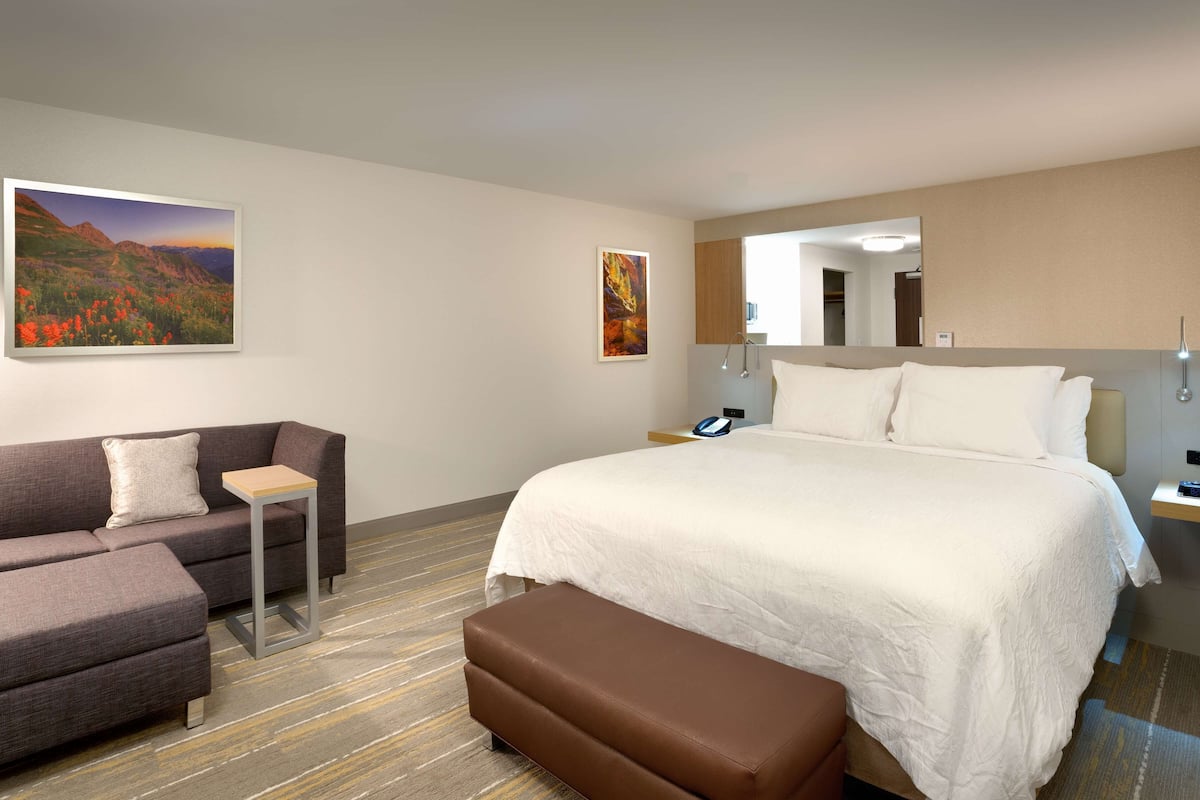 A hotel room with a bed, a sofa, a bench, a desk, a phone, and a mirror.