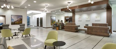 A hotel lobby with seating areas, a reception desk, and a view of the elevators.