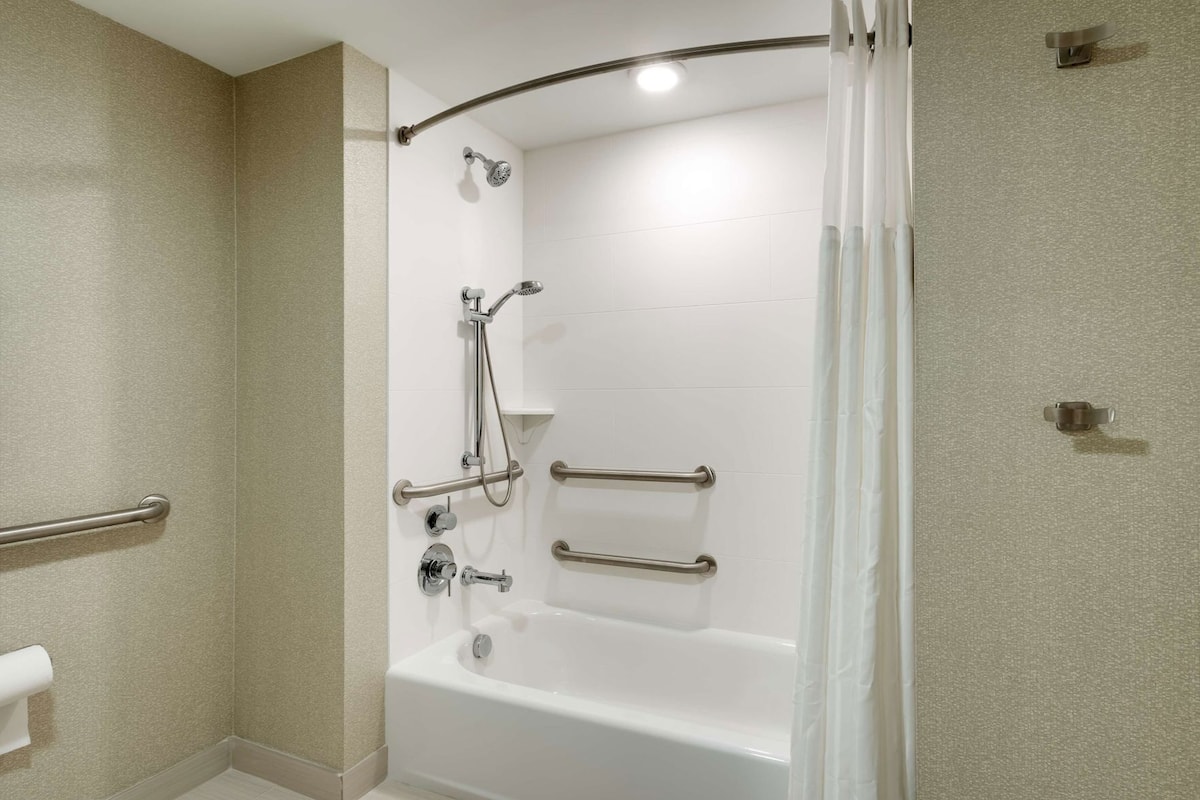 A bathroom with a bathtub, shower, grab bars, and a toilet paper holder.