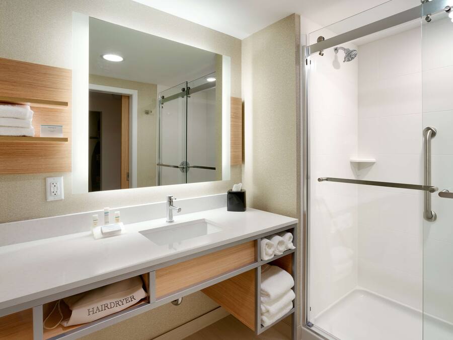 Un baño moderno con lavamanos blanco, espejo y ducha con mampara de vidrio.