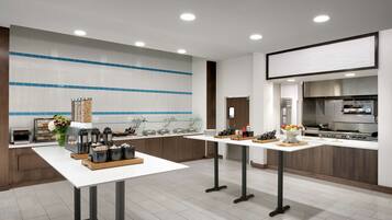 Een moderne keuken met een centraal eiland, een inbouwoven en een groot raam met zonwering.