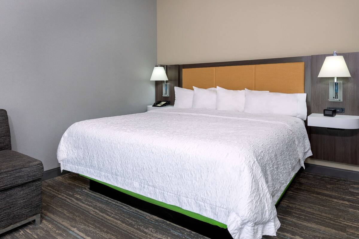A hotel room with a large bed, two bedside tables with lamps, a chair, and a carpeted floor.