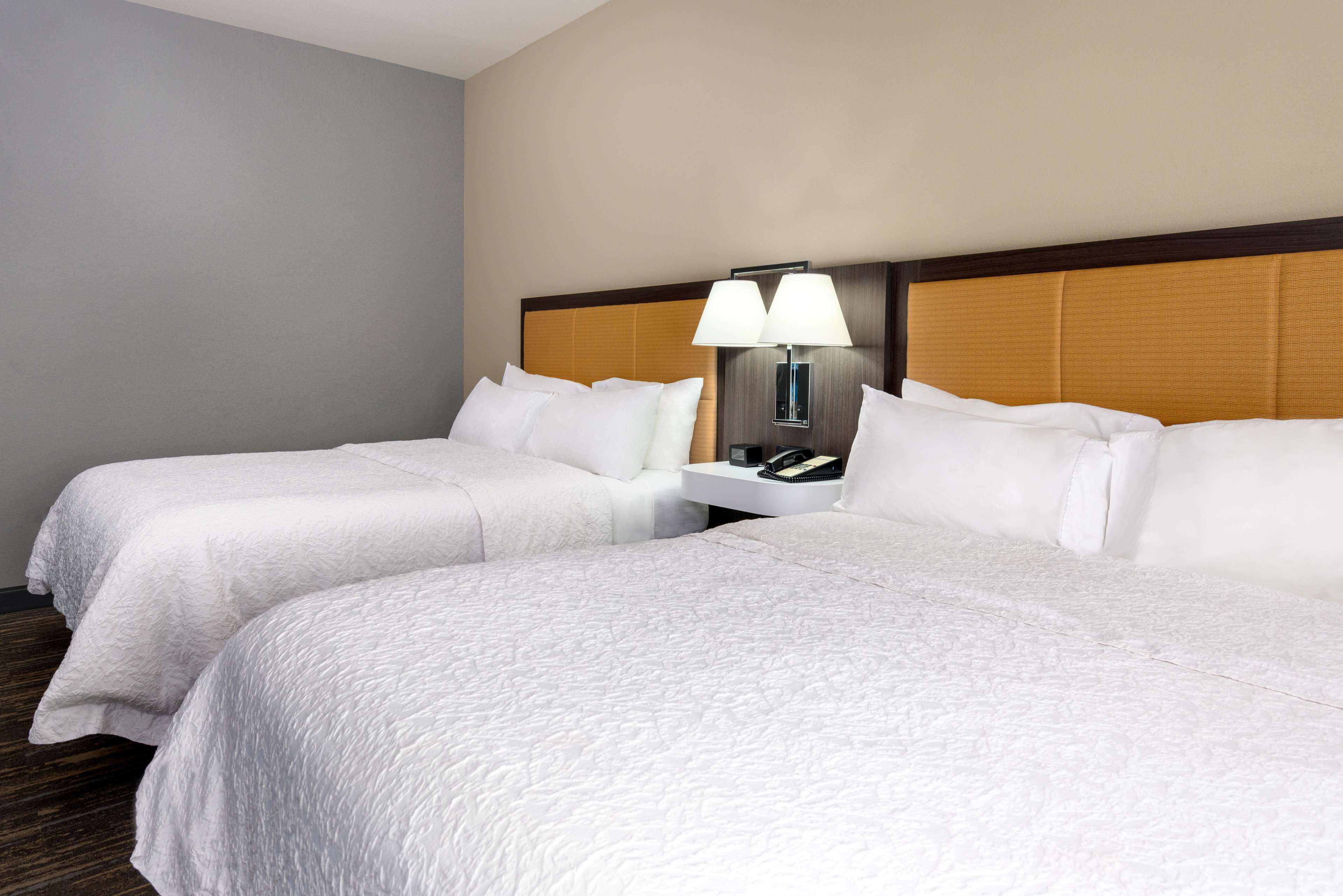 A hotel room with two beds, a nightstand with a lamp, and a telephone.