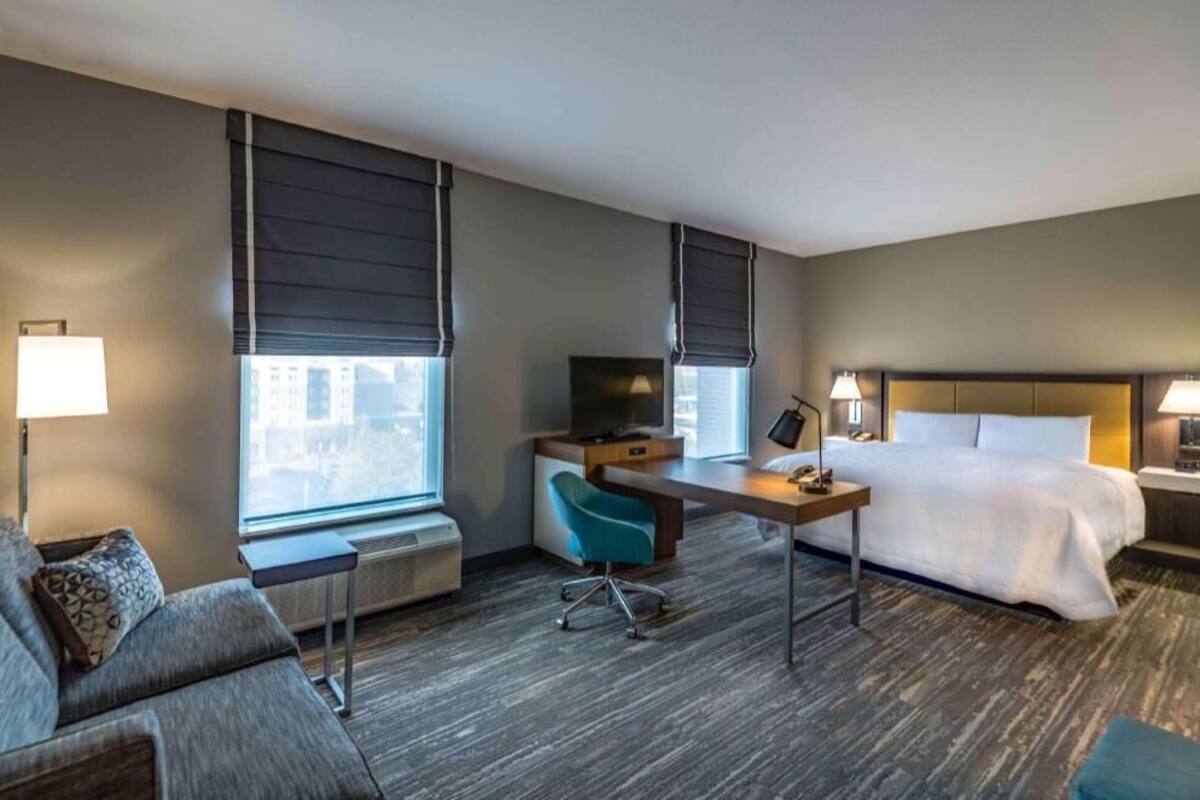 A hotel room with a bed, a desk, a chair, a TV, and a window.