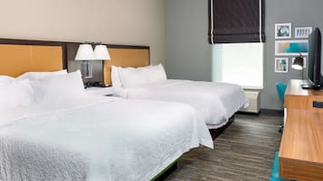 A hotel room with two beds, a desk, a chair, a TV, and a window with blinds.