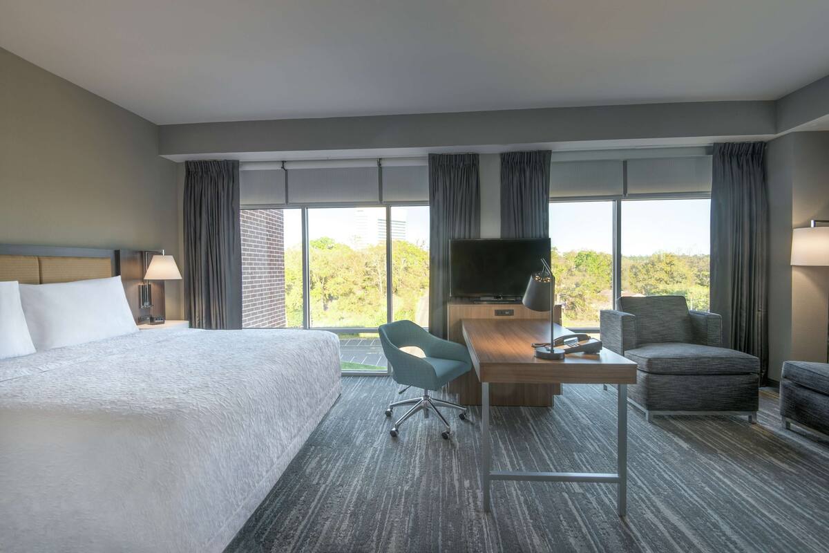 A hotel room with a large bed, a desk with a chair, a TV, and a view of the outdoors.