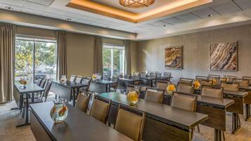 A conference room with multiple tables and chairs, large windows with curtains, and artwork on the walls.