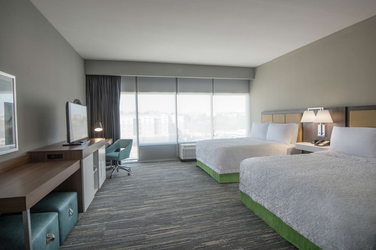 A hotel room with two beds, a desk, a chair, and a large window.