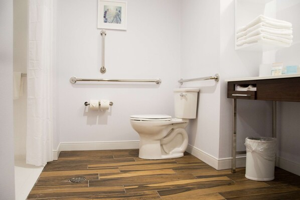 Un baño con inodoro blanco, suelo de madera, pasamanos, cubo de basura y perchero para toallas.