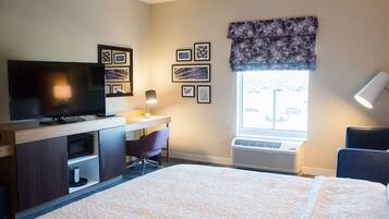 A hotel room with a bed, a desk with a television, a chair, a window with a view, and framed pictures on the wall.