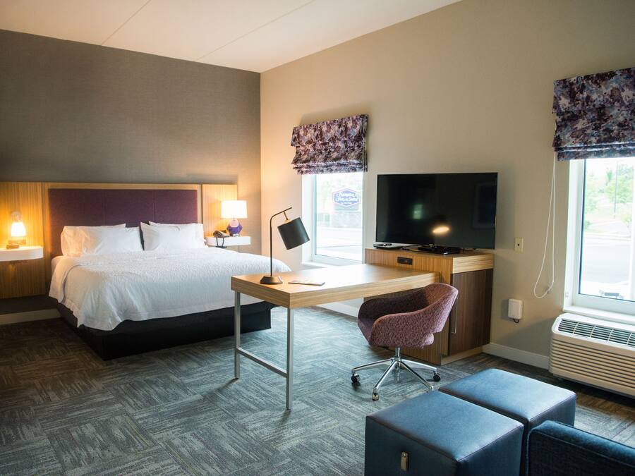 A hotel room with a bed, desk, chair, television, and a window with curtains.