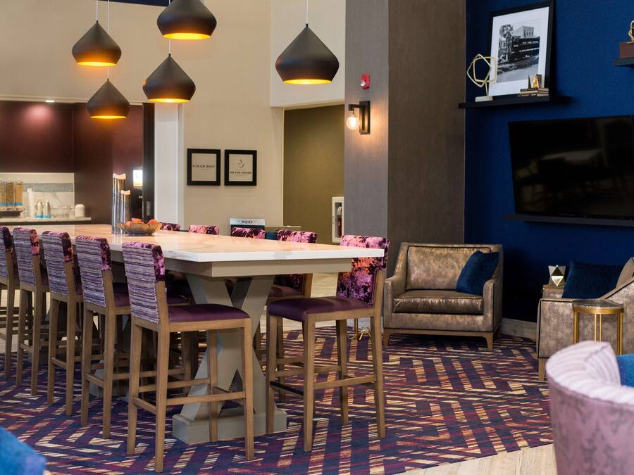 A hotel lobby with a long dining table, multiple chairs, a sofa, and a TV mounted on the wall.
