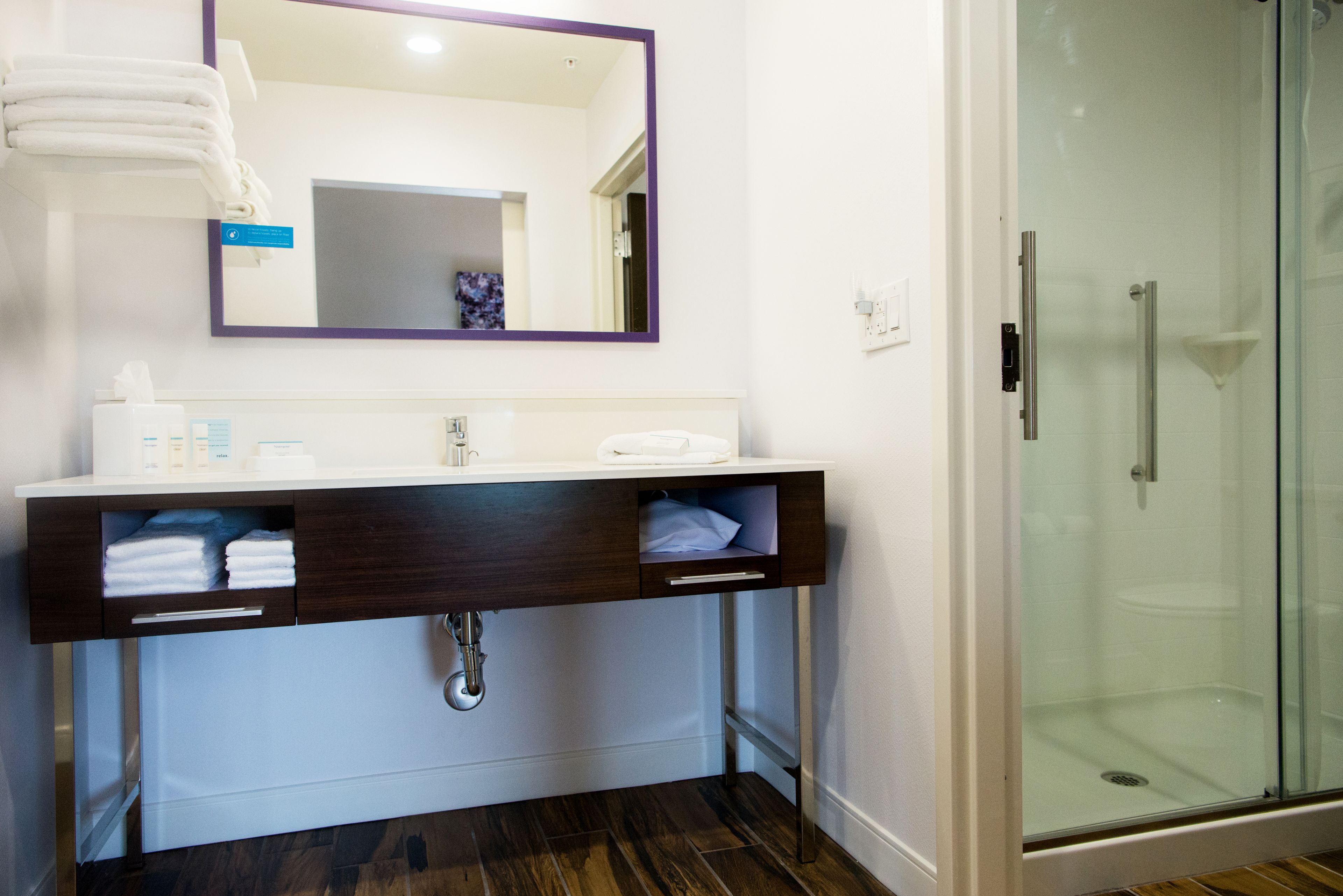 Un bagno con un mobile lavabo bianco, un armadietto in legno scuro e una cabina doccia in vetro.