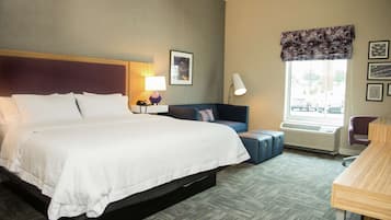 A hotel room with a large bed, a desk, a chair, a window with a view, and a wall-mounted air conditioner.