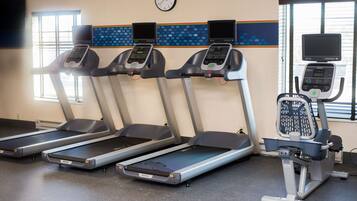 Quatre tapis de course et un appareil elliptique dans une salle de sport, avec une horloge au mur.