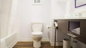 Un baño con inodoro, lavamanos, espejo y un cubo de basura.