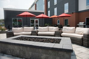 An outdoor seating area with a fire pit, wicker furniture, and red umbrellas. - Hampton Inn & Suites by Hilton Warrington Horsham (Warrington)
