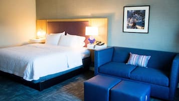 A hotel room with a bed, a blue sofa, and a small table with a lamp.