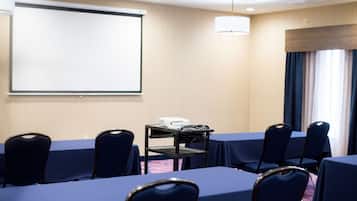 Un salón de conferencias con mesas, sillas, un proyector y una pantalla.