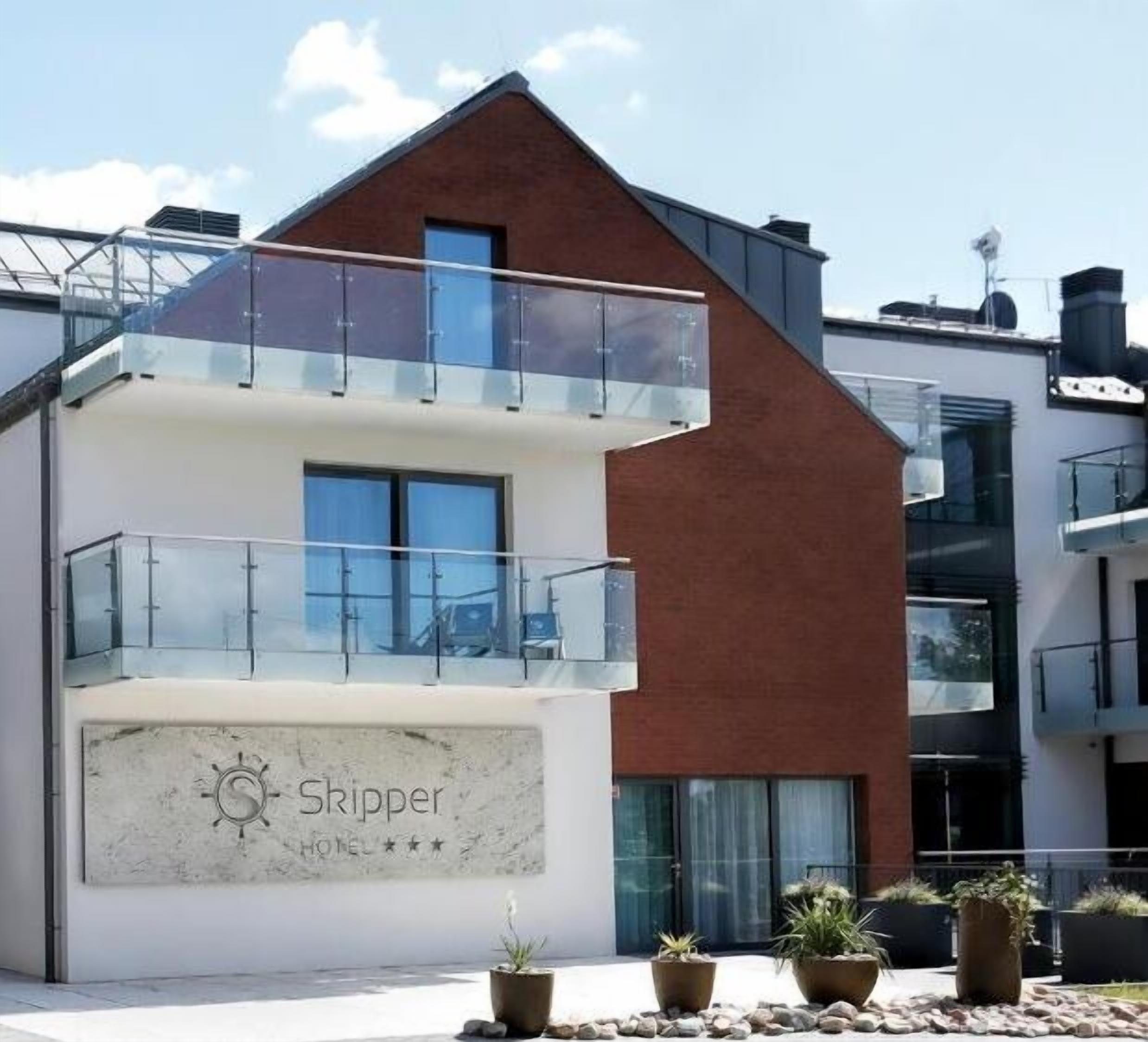 A modern hotel with a prominent 'Skipper' sign, a balcony, and potted plants in the foreground.