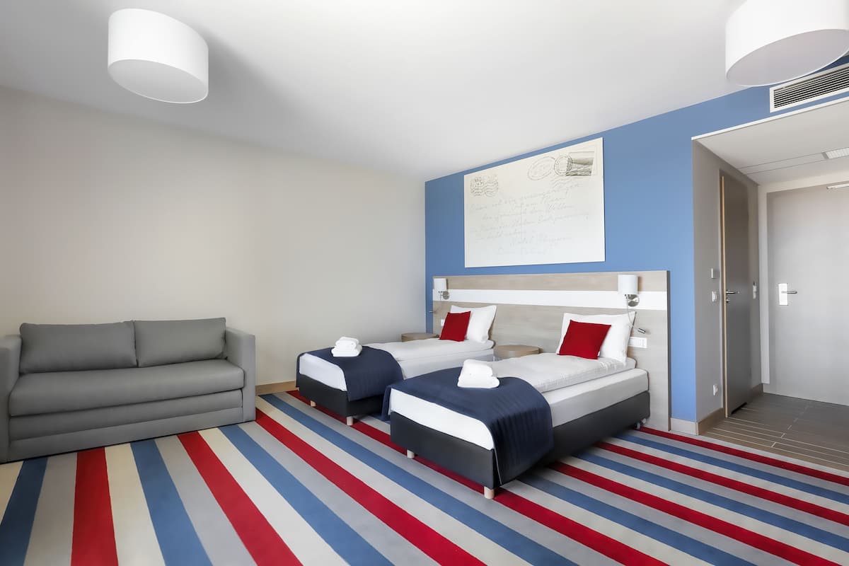 A hotel room with two beds, a sofa, a striped carpet, and a wall-mounted artwork.