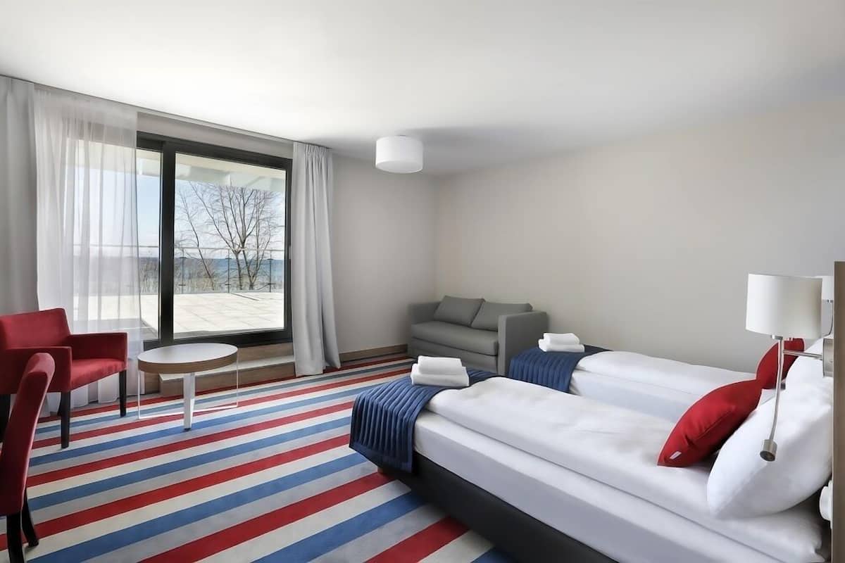 A hotel room with a large window, a sofa, a bed, and a small table.