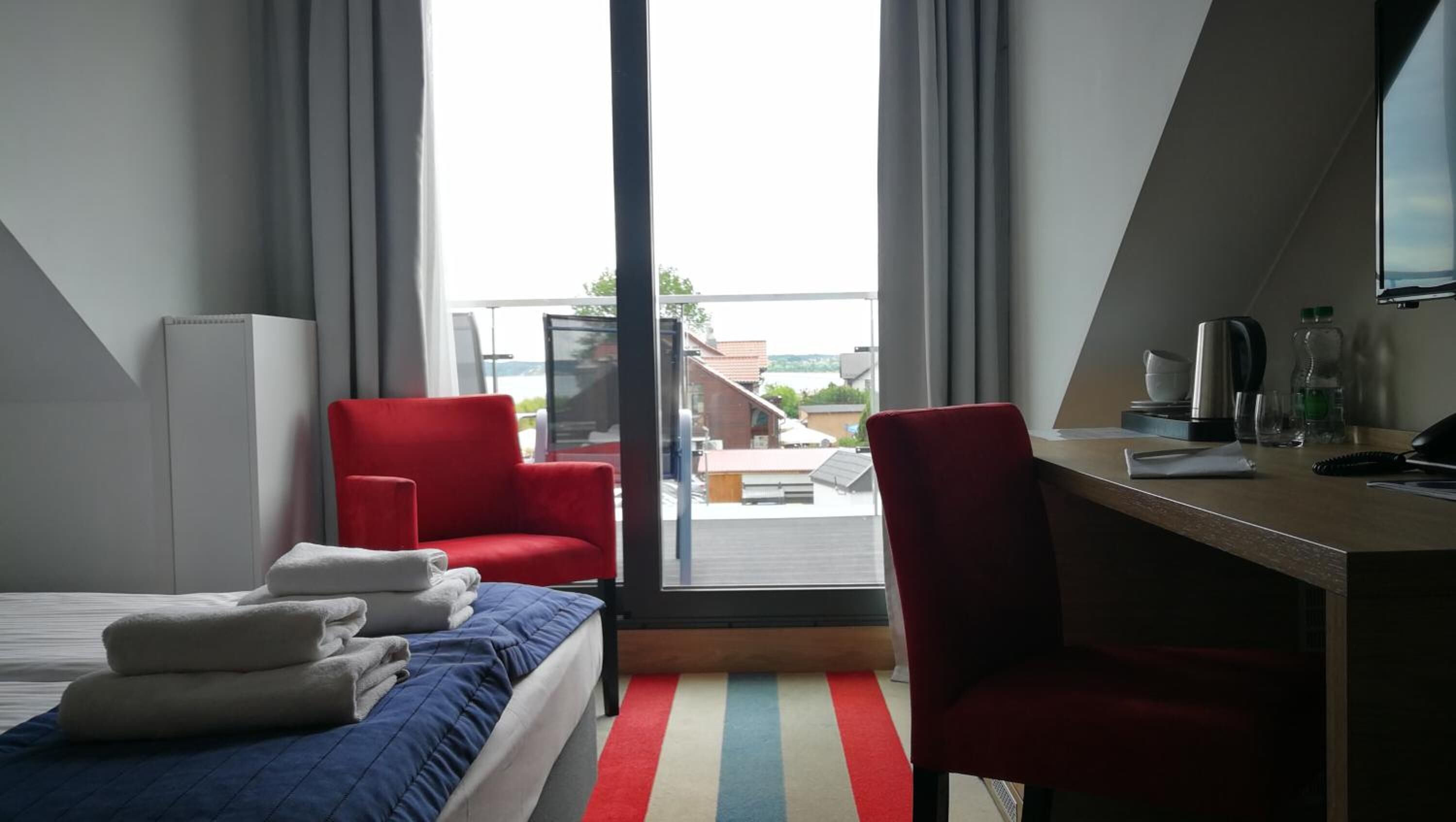 A hotel room with a bed, a desk, a chair, and a view of the outside.