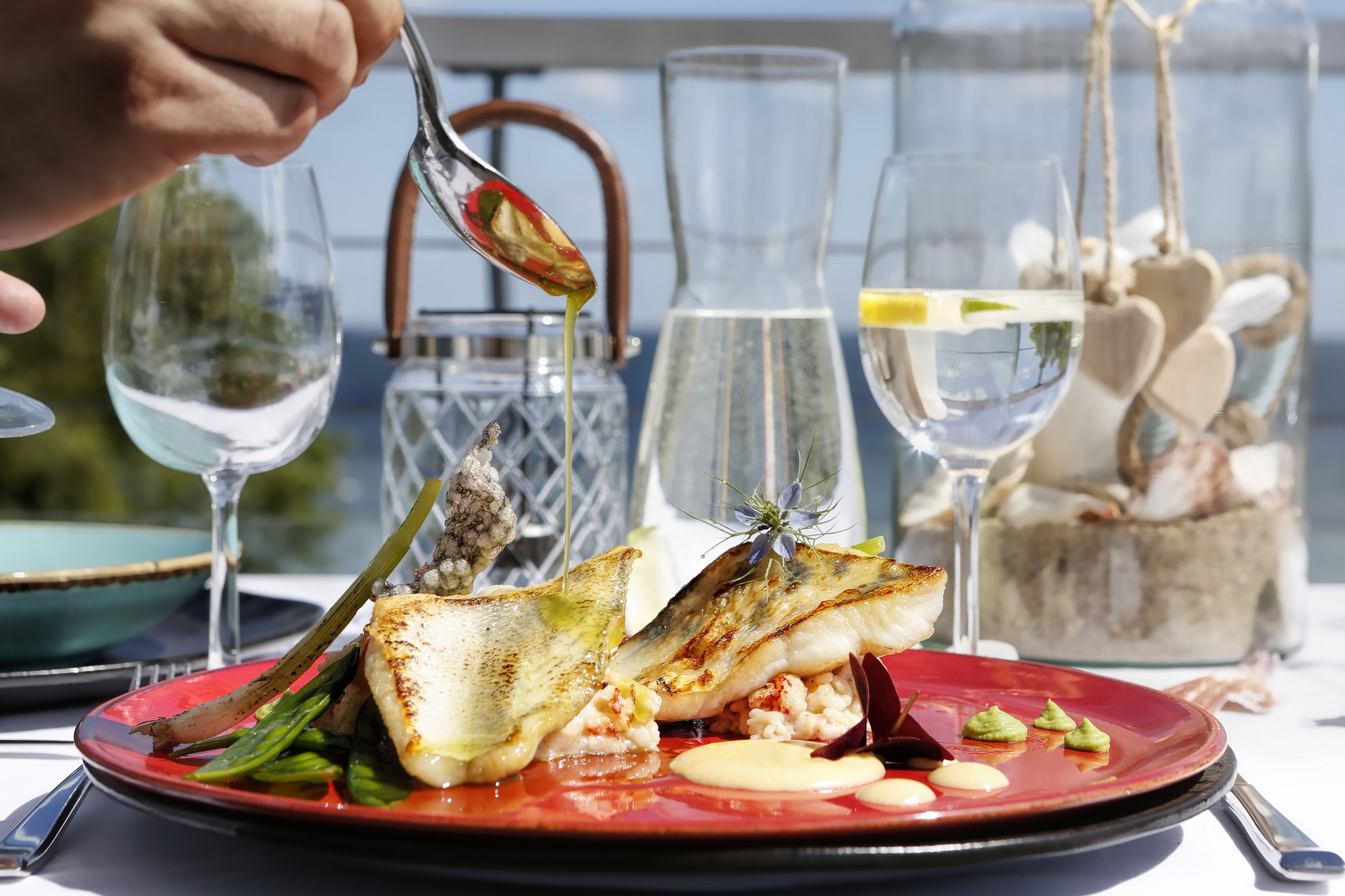 A meal with a red plate, a glass of white wine, and a clear glass with a yellow garnish.