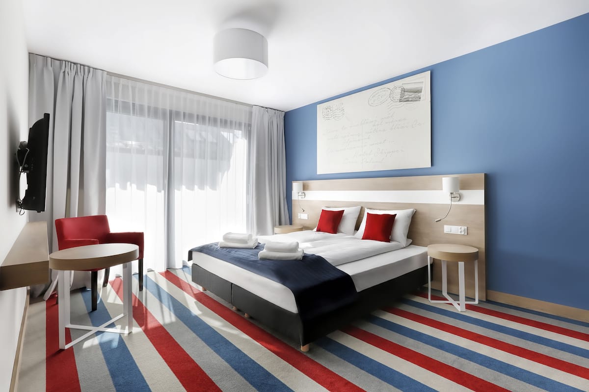 A modern hotel room with a large bed, a desk, a chair, and a view of the city.